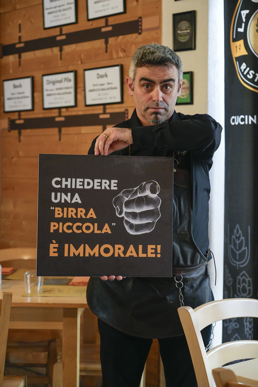 Pulcherio Scutti con cartello 'Chiedere una birra piccola è immorale'